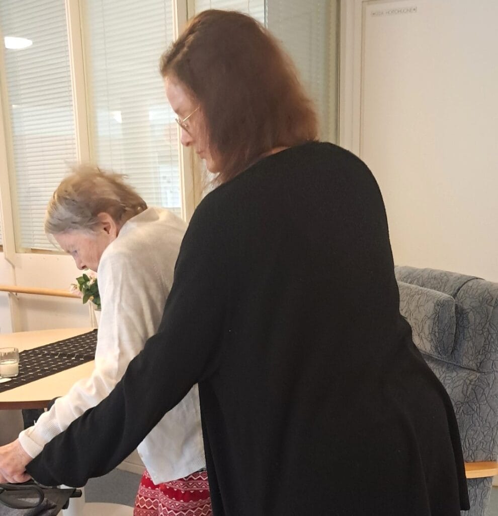 Hoitaja auttaa ikääntynyttä rollaattorin kanssa.